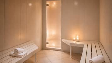 Un cuarto de sauna con bancos y una mesa, una puerta que da a una zona de ducha y velas sobre la mesa.