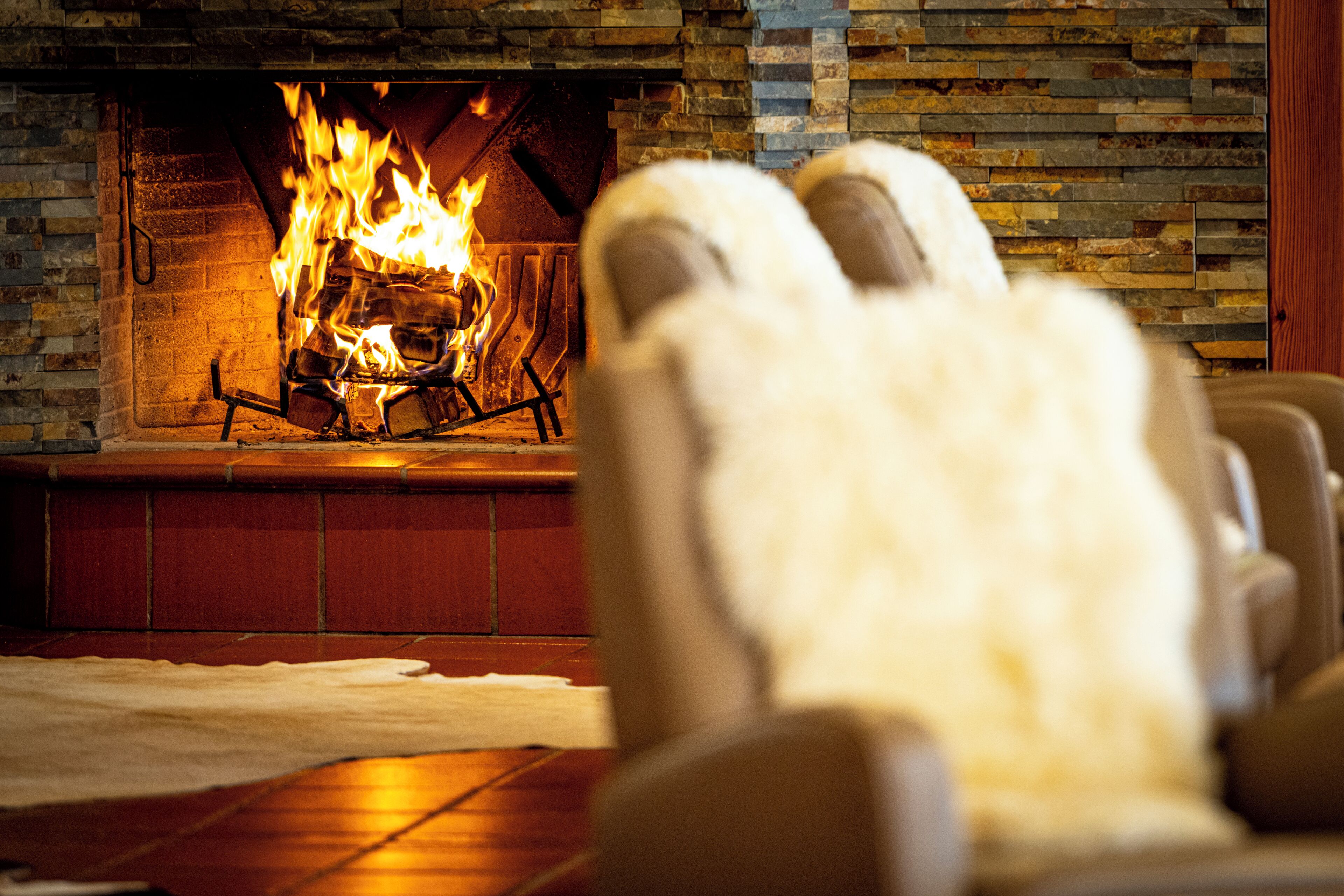 A fireplace with a fire, a white fur rug, and a wooden floor.