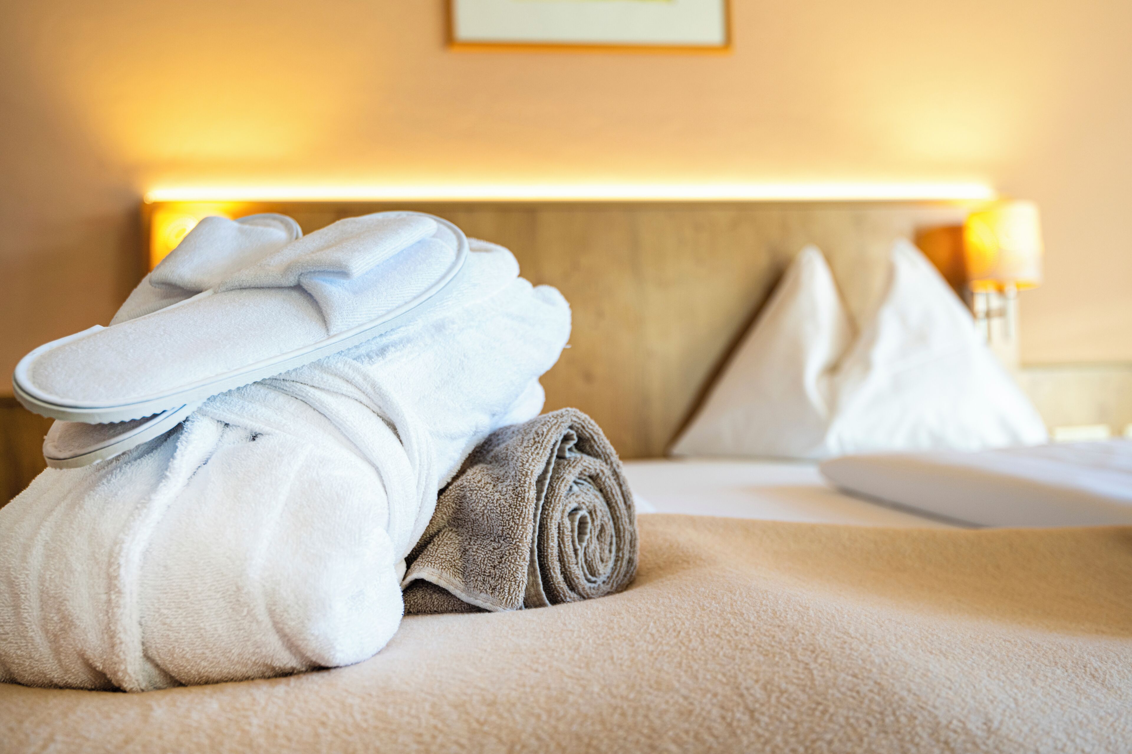 A neatly made bed with a folded towel and a rolled-up towel on a textured beige bedspread.