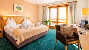 Una habitación de hotel con cama, una silla, un escritorio, una planta y una ventana con cortinas.