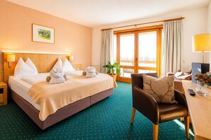 Una habitación de hotel con cama, una silla, un escritorio, una planta y una ventana con cortinas.