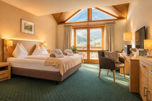 Habitación de hotel con cama, escritorio, silla, televisor y una ventana grande con vistas a la montaña.