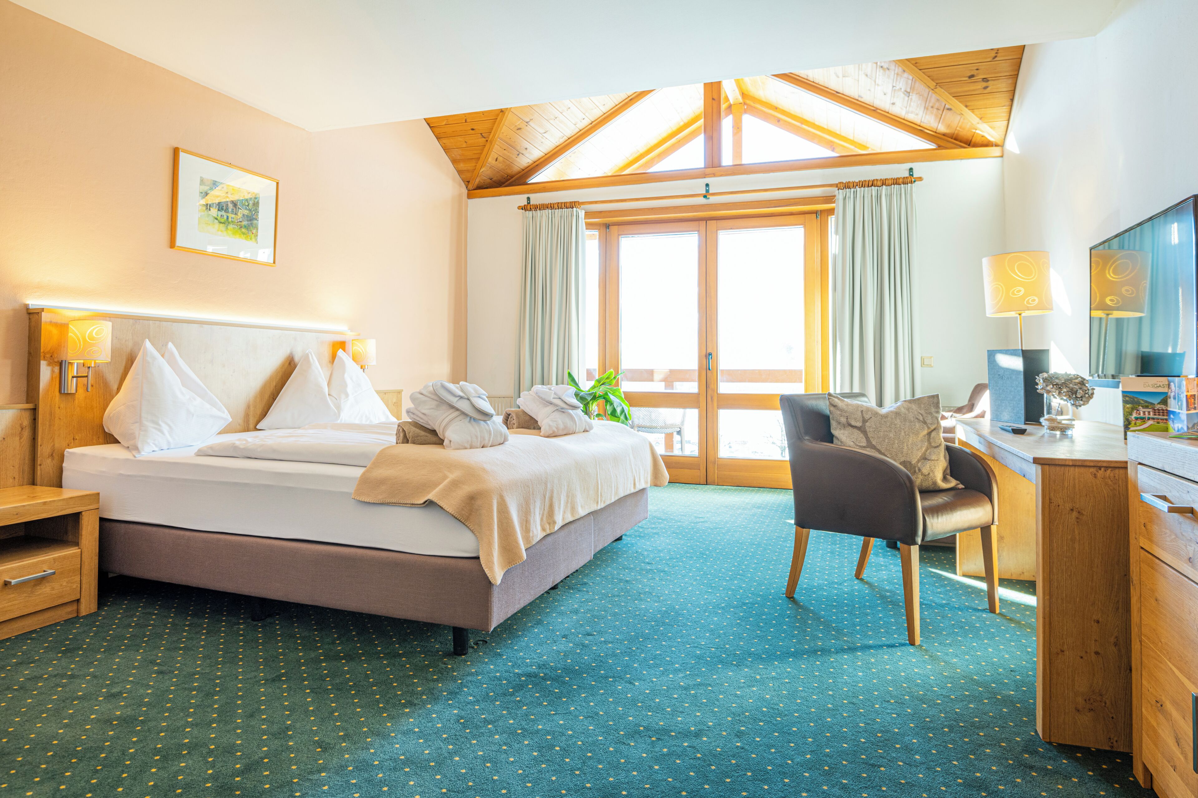 A hotel room with a bed, desk, chair, and a large window with curtains.