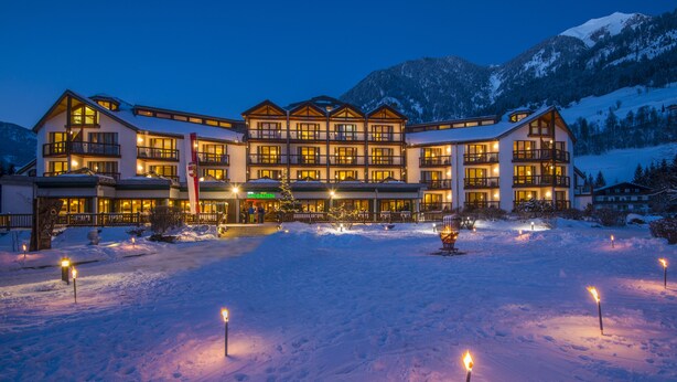 Un hotel grande de varios pisos con un patio cubierto de nieve y ventanas iluminadas.