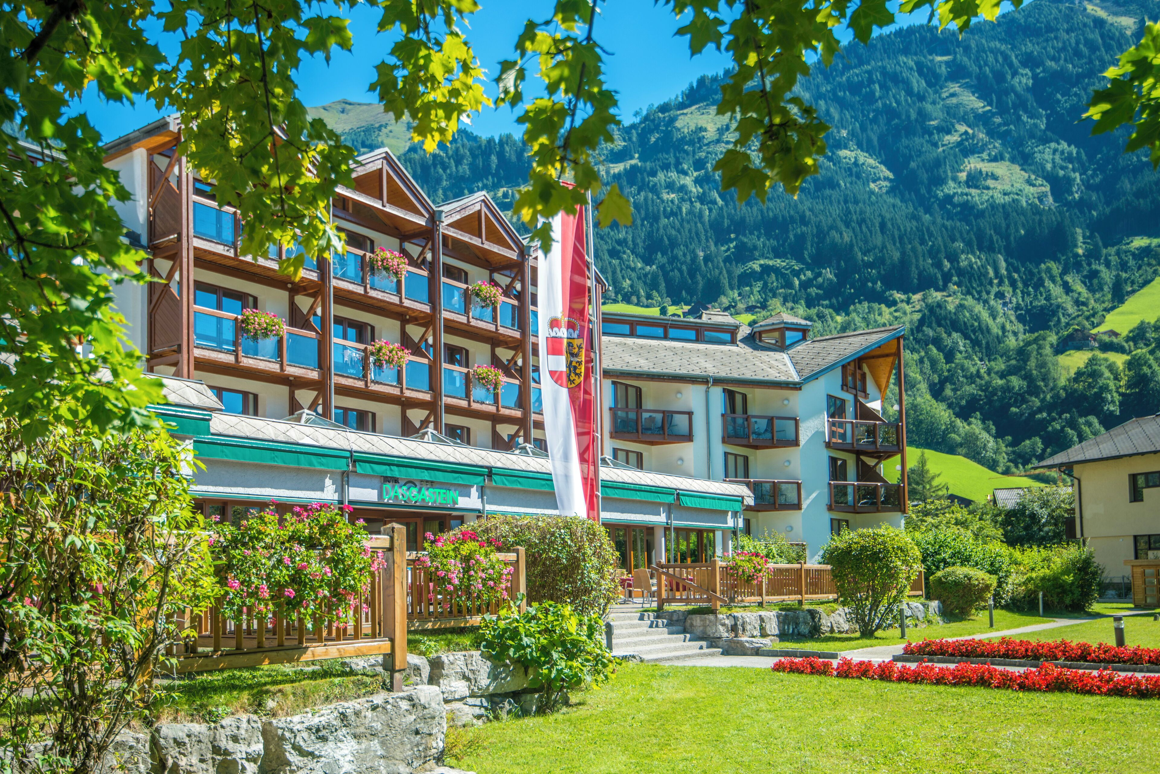 Un hotel con varios balcones, una bandera y montañas al fondo.