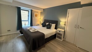 A bedroom with a bed, two bedside tables, a wardrobe, a window with curtains, and a wall-mounted picture. - Clyde Waterfront Apartments (Glasgow)