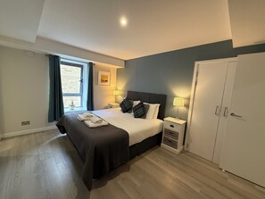 Ein Schlafzimmer mit einem Bett, zwei Nachttischen, einem Kleiderschrank, einem Fenster mit Vorhängen und einem an der Wand hängenden Bild.