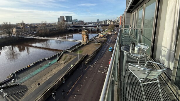 A high vantage point view of a riverside promenade with a bridge, modern buildings, and a clear sky. - Clyde Waterfront Apartments (Glasgow)