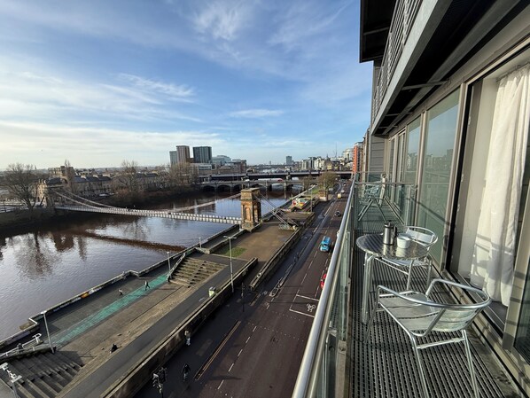 Blick von oben auf eine Uferpromenade mit einer Brücke, modernen Gebäuden und einem klaren Himmel.