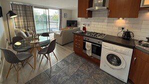 A modern kitchen with a stove, oven, and washing machine, a dining area with chairs and a table, and a sofa. - Clyde Waterfront Apartments (Glasgow)