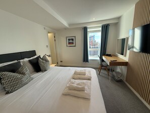 A hotel room with a bed, a desk, a chair, a TV, and a window with curtains. - Clyde Waterfront Apartments (Glasgow)