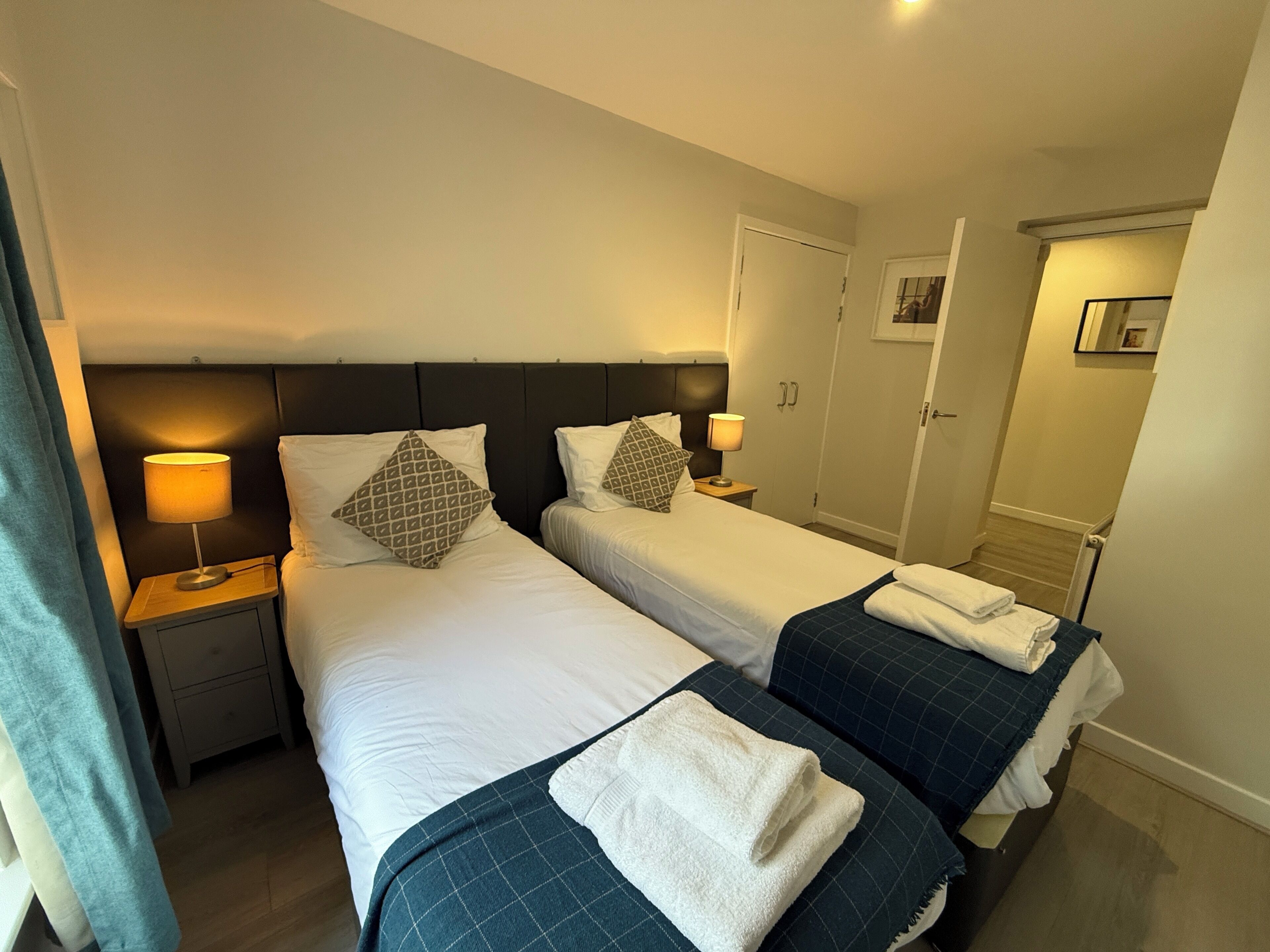A hotel room with two beds, nightstands with lamps, a door, and a small picture on the wall.