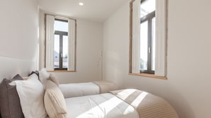 A bedroom with two beds, a window, and a shelf with items. - BO - Marquês Apartments (Porto)