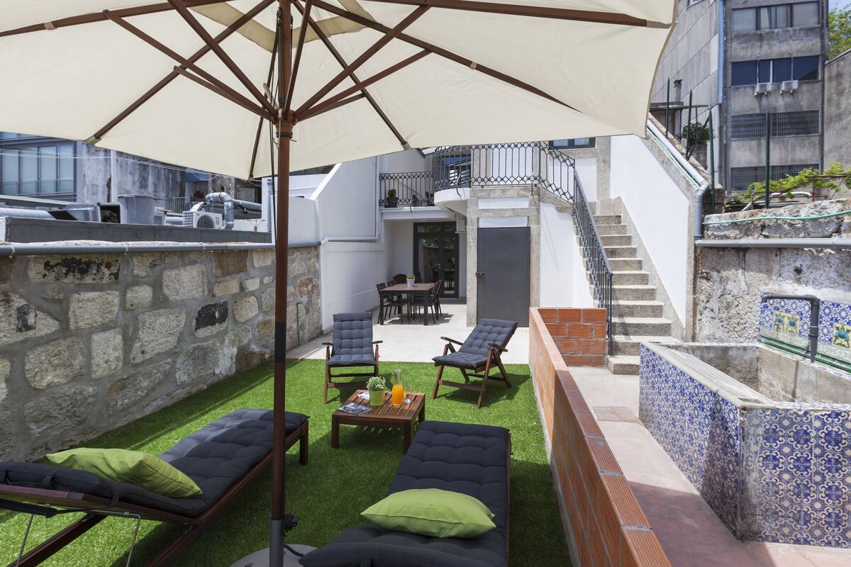A rooftop patio with outdoor furniture, a pergola, and a view of a building with a staircase.