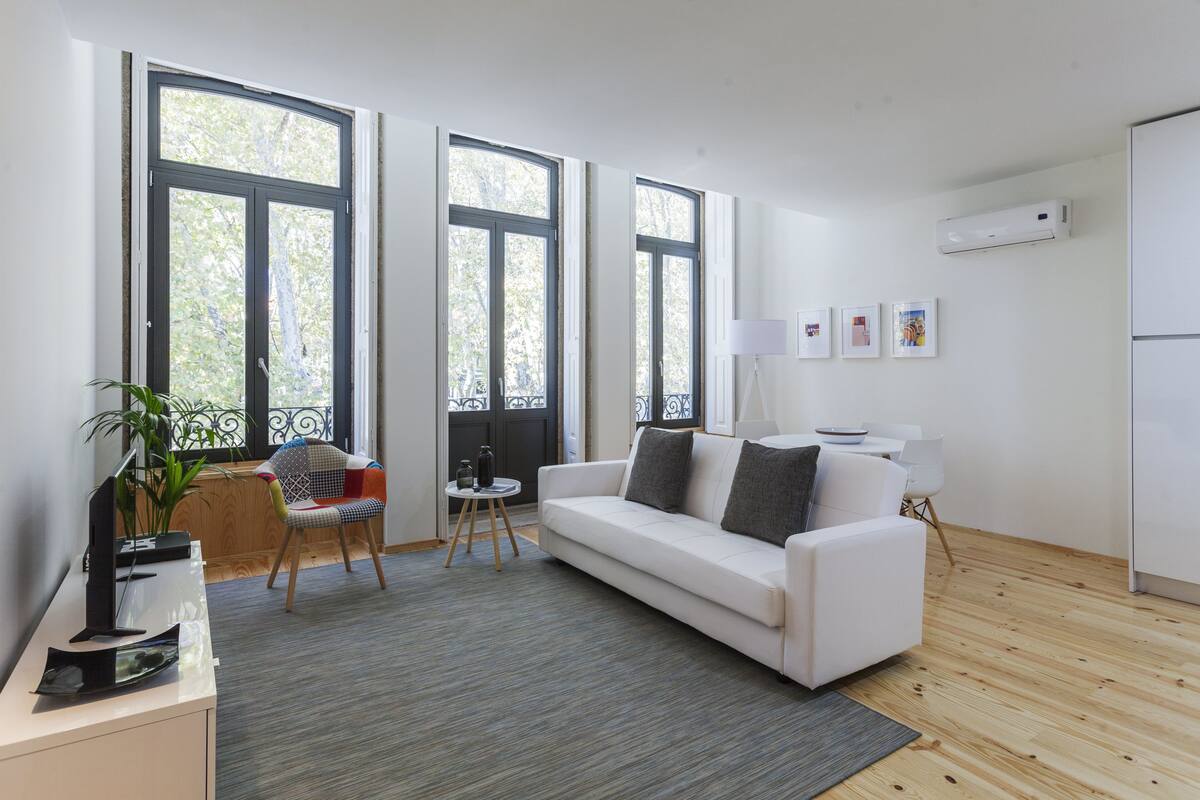 A modern living room with a white sofa, a small side table, a chair, and a large window with a view of trees.
