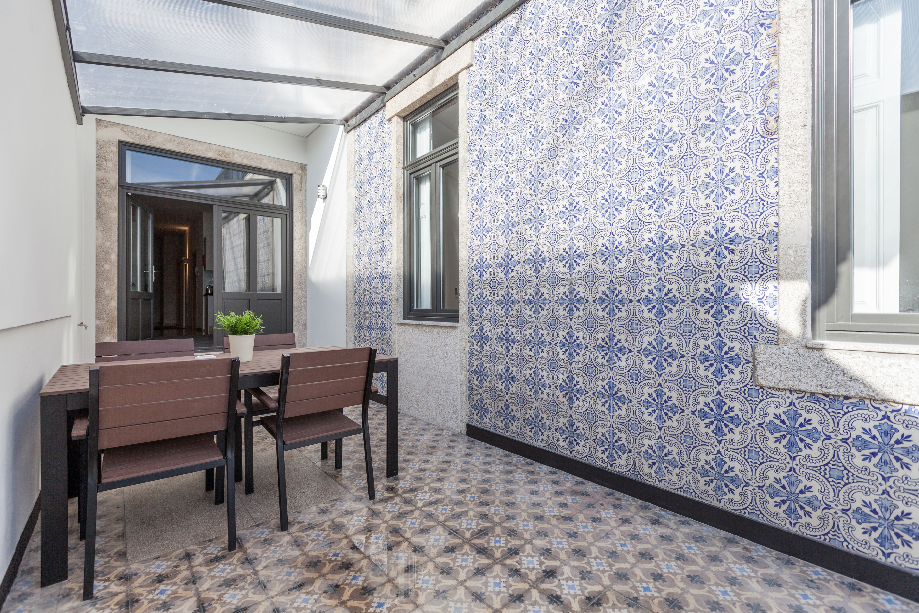 A patio with a table and chairs, a potted plant, and patterned tiles.