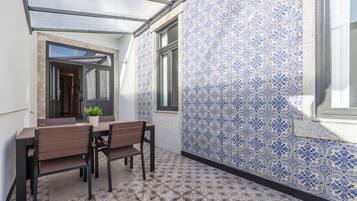 A patio with a table and chairs, a potted plant, and patterned tiles.