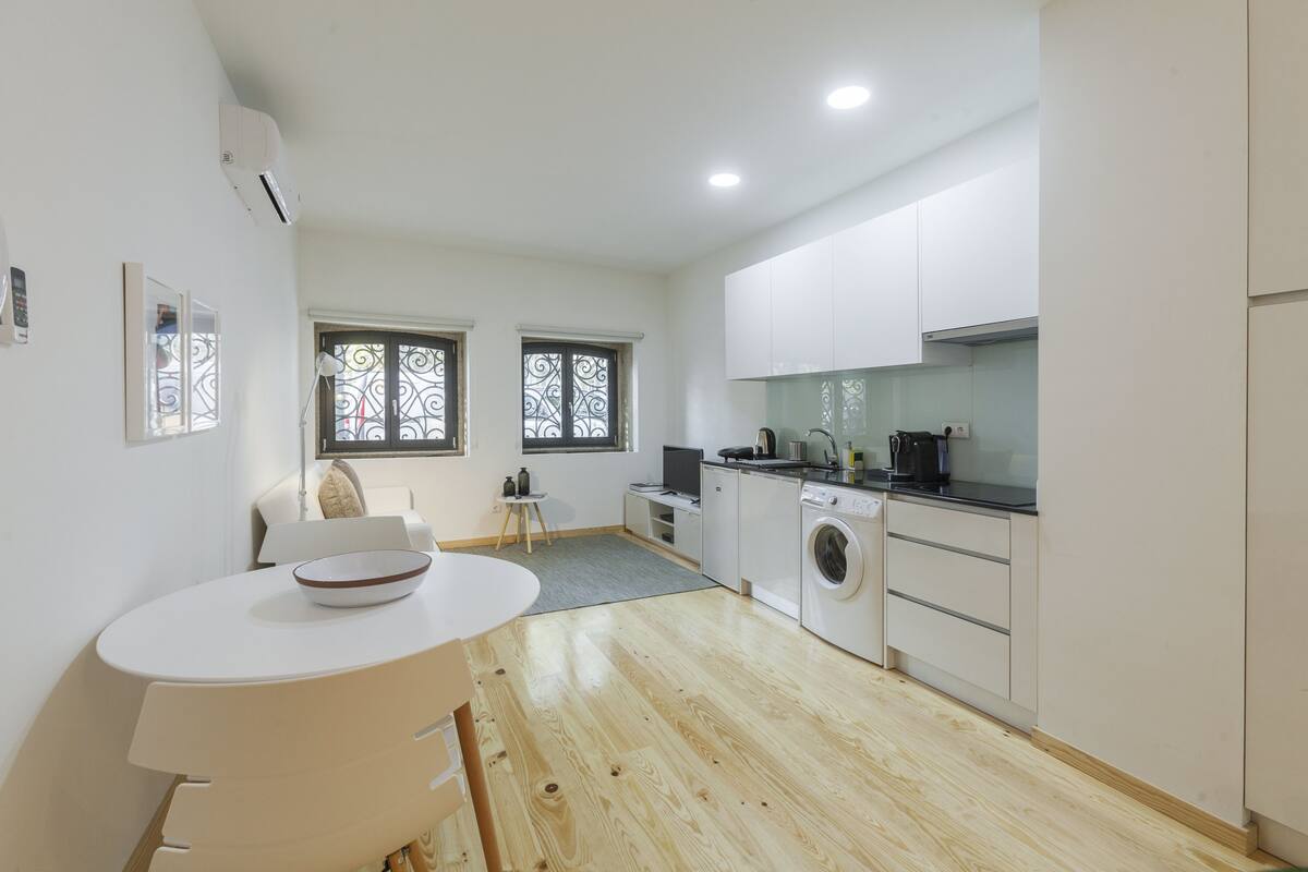 A modern kitchen with white cabinets, a washing machine, and a dining area with a table and chairs.