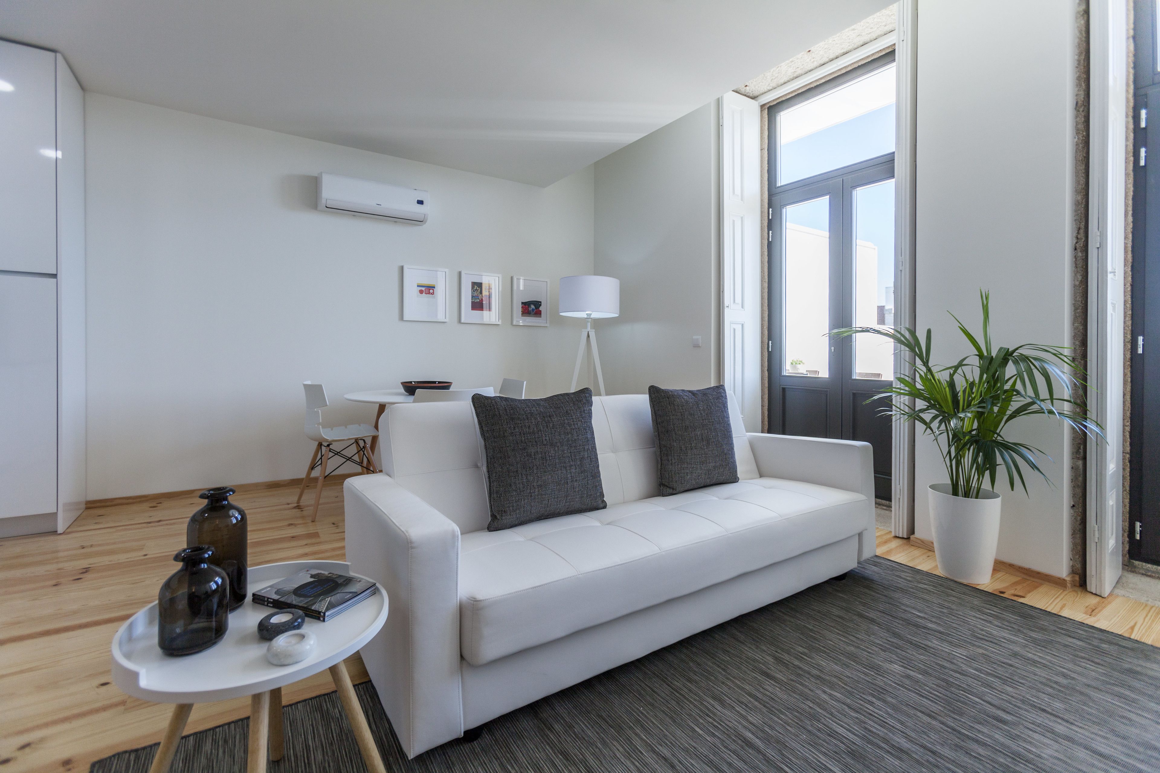 A modern living room with a white sofa, a small round table with decorative items, a floor lamp, and a potted plant.