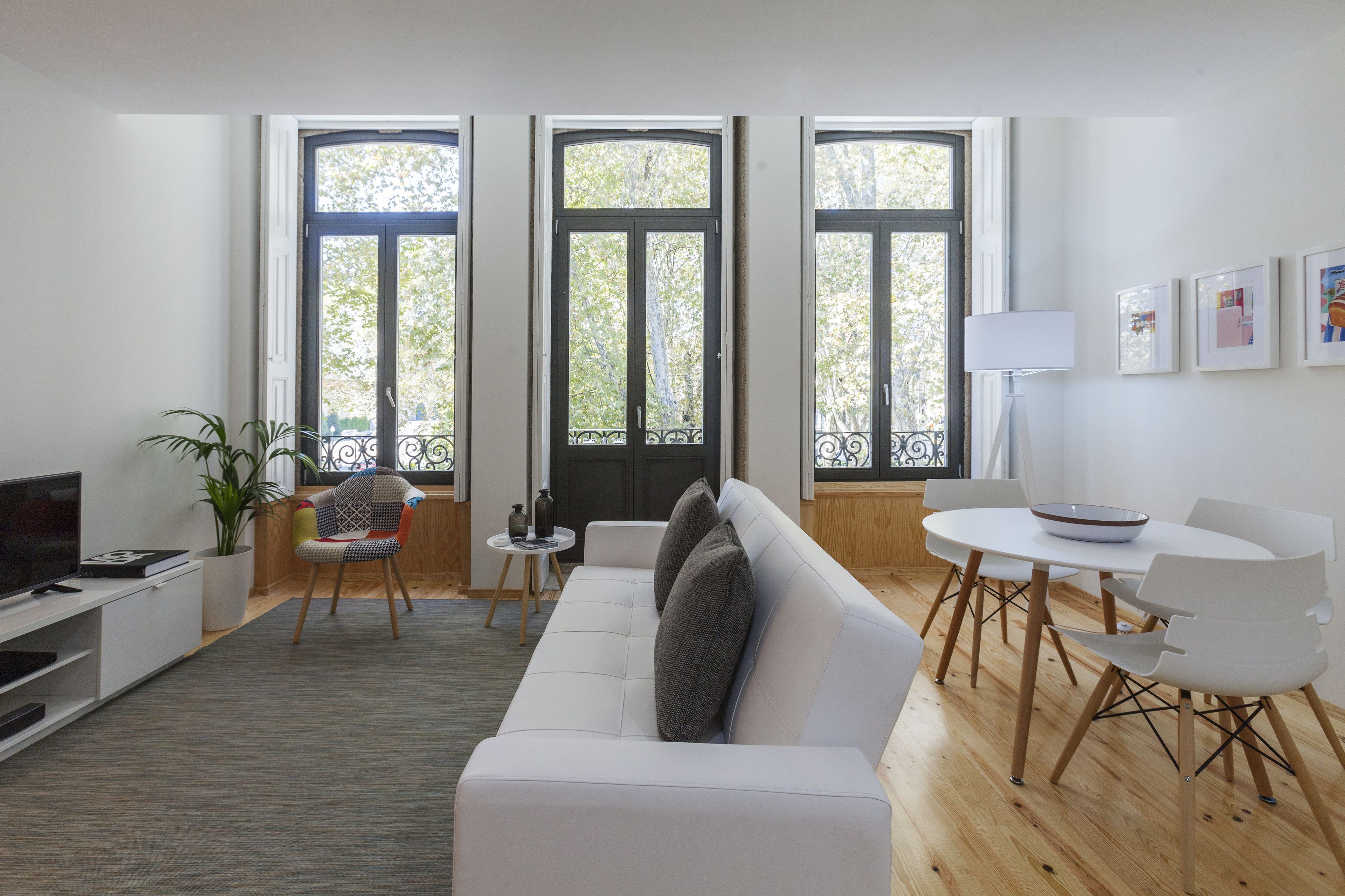 A modern living room with a white sofa, a dining table with chairs, a TV, and a potted plant.