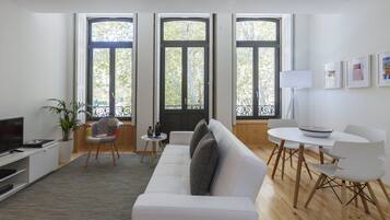A modern living room with a white sofa, a dining table with chairs, a TV, and a potted plant.