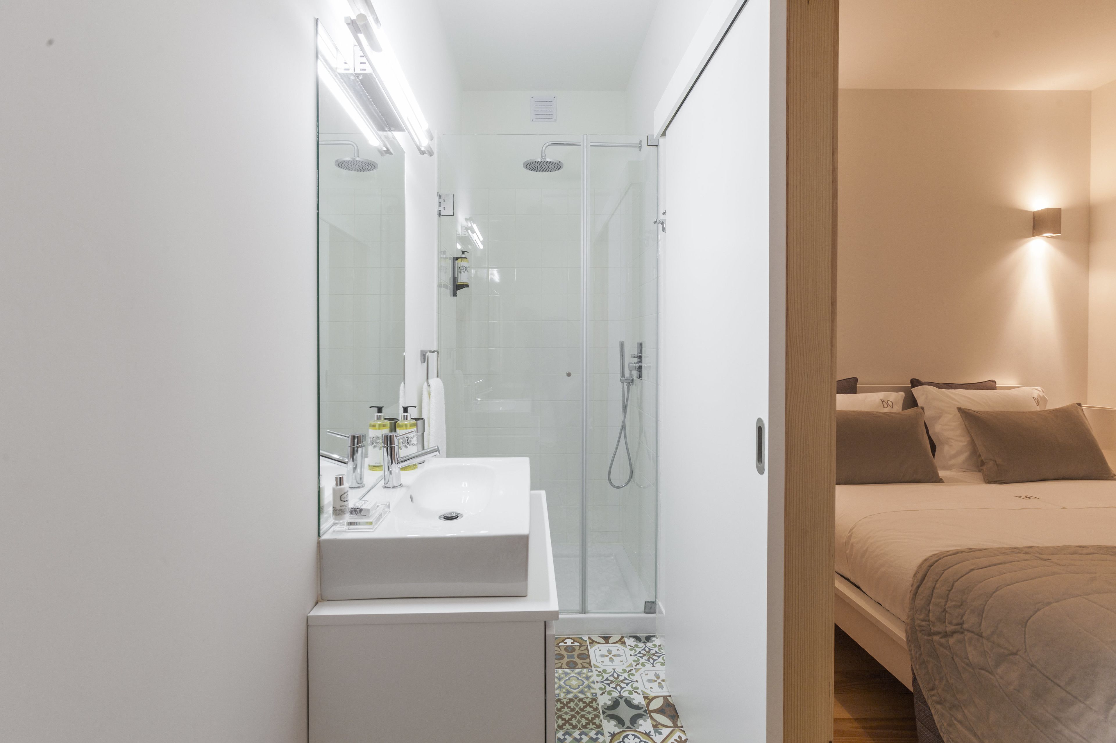 Un baño moderno con ducha de vidrio, un lavamanos blanco y una mesita de noche.