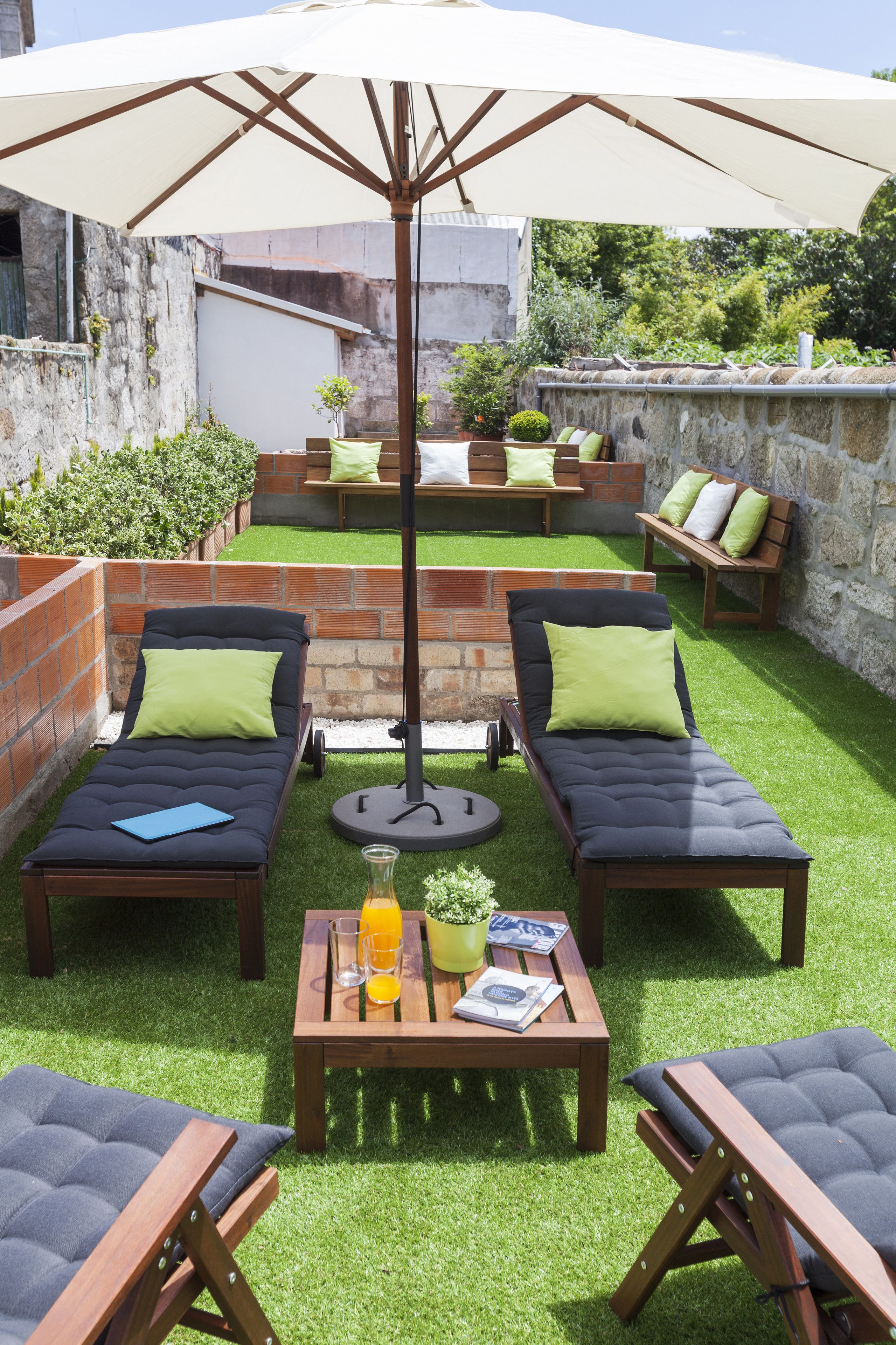 A patio with two lounge chairs, a table with drinks, and a large umbrella.