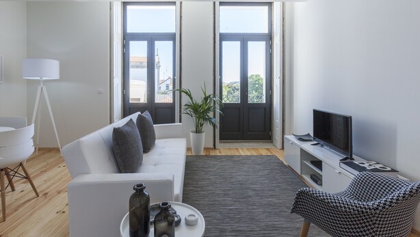 A modern living room with a white sofa, a television on a white stand, a patterned chair, and a potted plant. - BO - Marquês Apartments (Porto)