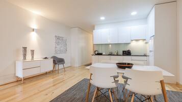 Een moderne keuken met witte kastjes, een eethoek met een witte tafel en stoelen, en een grijze vloerkleed.