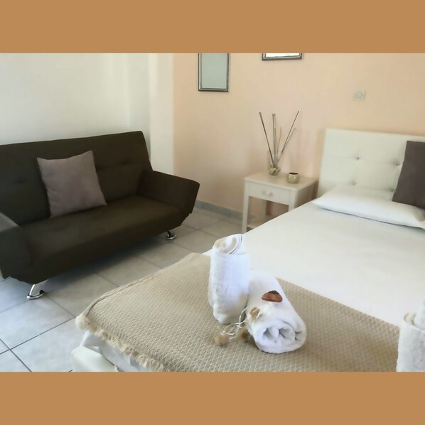A hotel room with a bed, a sofa, a small table with a vase, and a wall-mounted picture frame. - Zante Flower (Zakynthos)