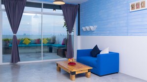 Una sala de estar moderna con un sofá azul, una mesa de centro de madera y un amplio ventanal corredero que da a un espacio exterior.