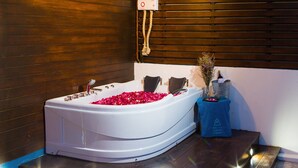 Un baño moderno con una bañera independiente llena de pétalos de rosa, una pared de madera y una pequeña mesa con un jarrón de flores y una botella de champán.