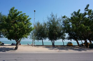 A beach with trees, a street, and a yellow taxi. - Chaamaran Boutique Hotel (Cha-am)