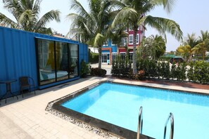A swimming pool with a blue interior, surrounded by palm trees and a blue building with large windows.