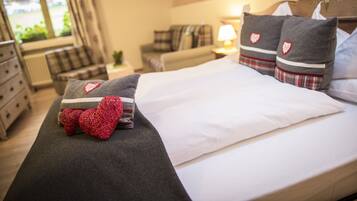 A neatly made bed with a white comforter and two pillows with heart designs.