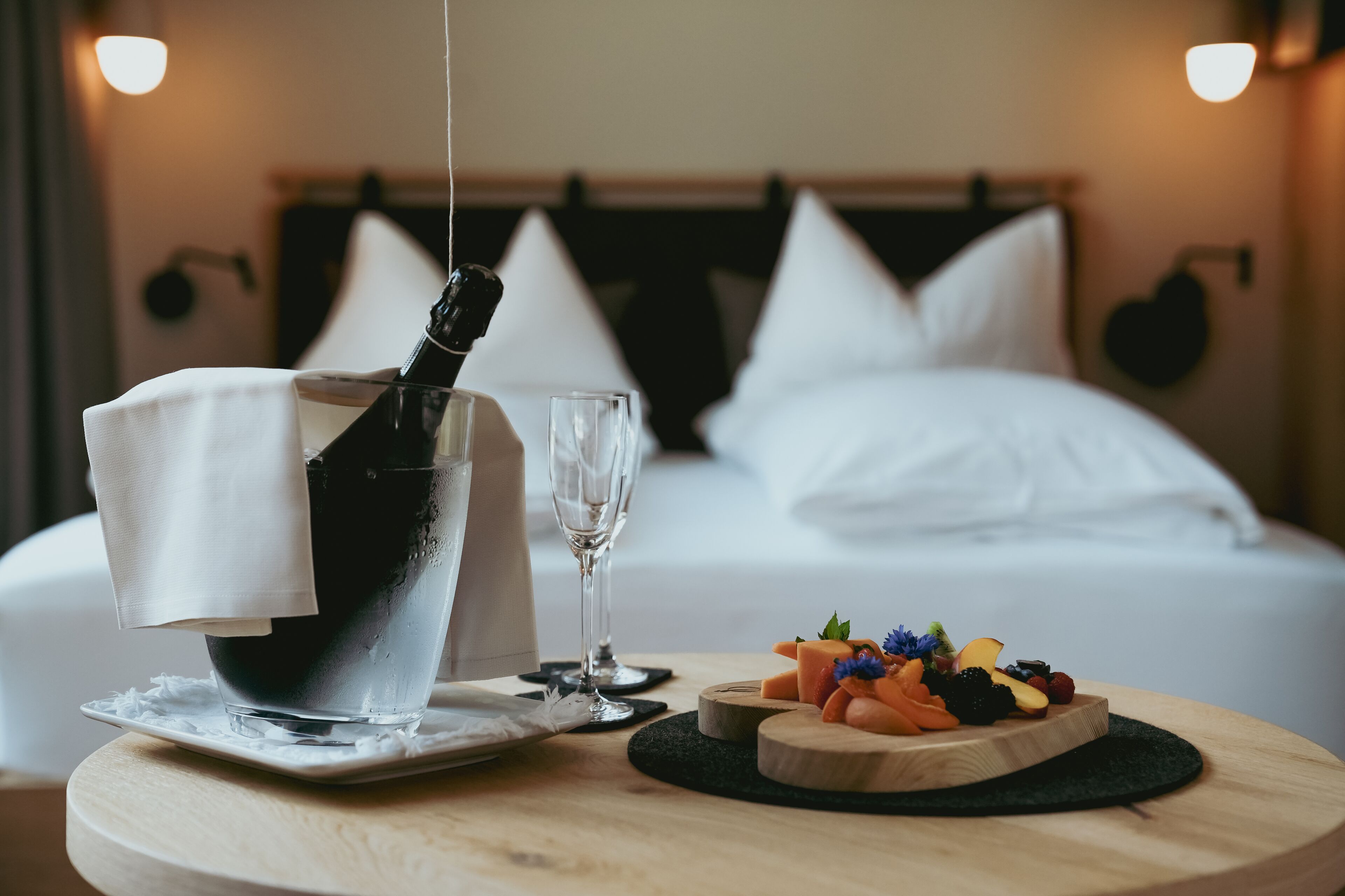 A neatly arranged breakfast setting with a bottle of champagne, a glass, and a fruit platter on a round wooden table.