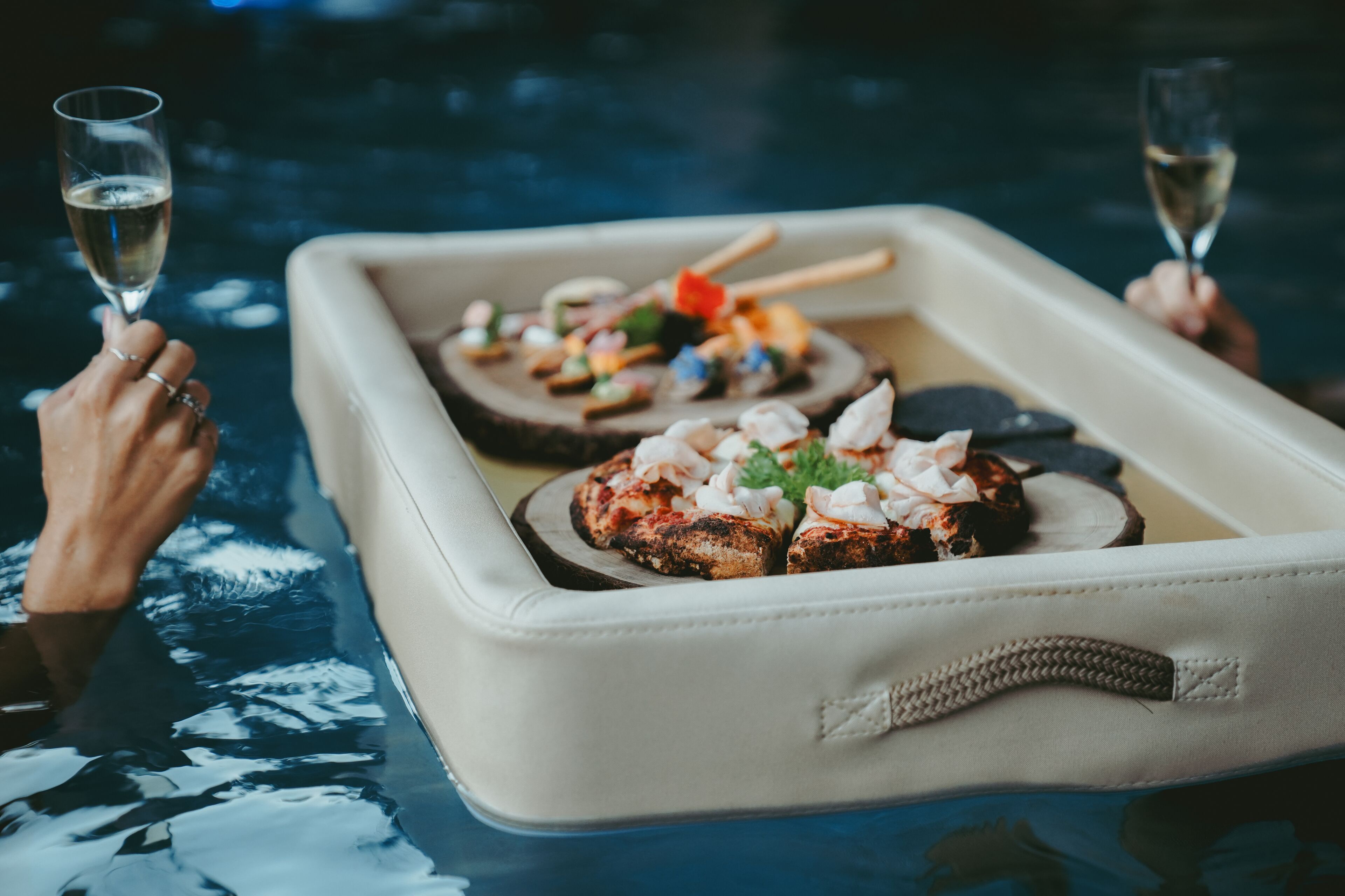A tray with food items and two glasses of a clear liquid, likely wine, on a reflective surface.