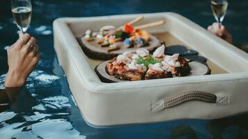 A tray with food items and two glasses of a clear liquid, likely wine, on a reflective surface.