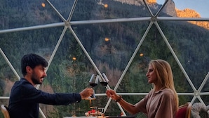 Un couple déjeune à l’intérieur d’une coupole géodésique, avec vue sur la montagne.