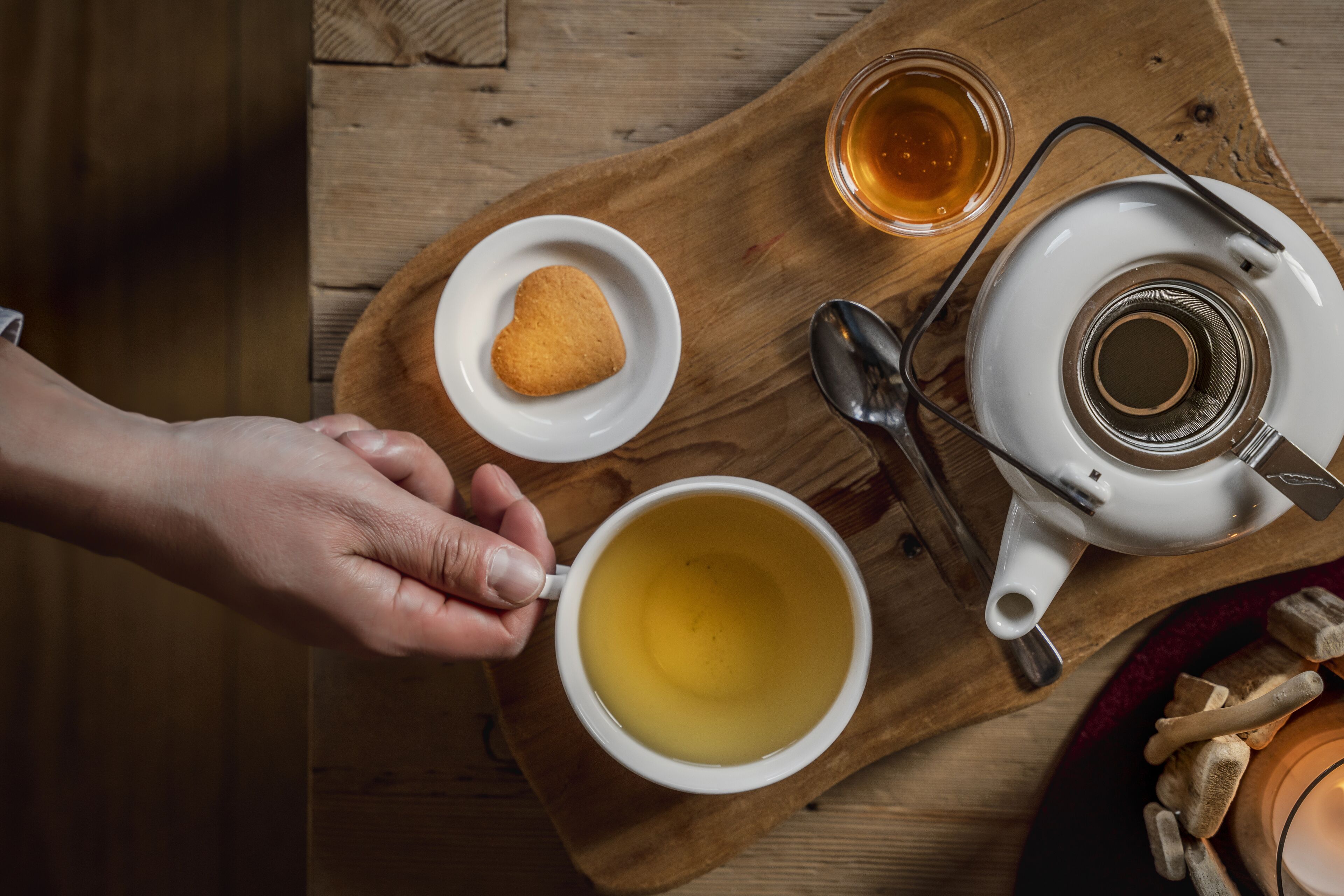 A wooden tray with a teapot, a cup of tea, a small plate with a cookie, and a glass of tea.