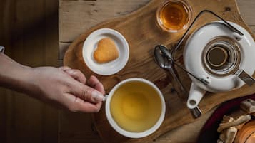 A wooden tray with a teapot, a cup of tea, a small plate with a cookie, and a glass of tea.