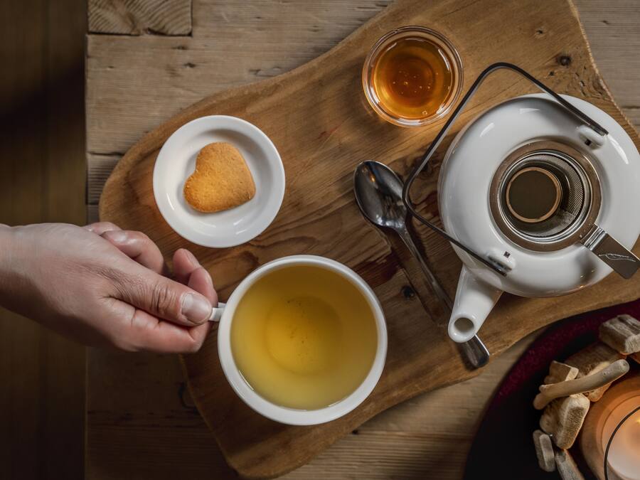 A wooden tray with a teapot, a cup of tea, a small plate with a cookie, and a glass of tea.