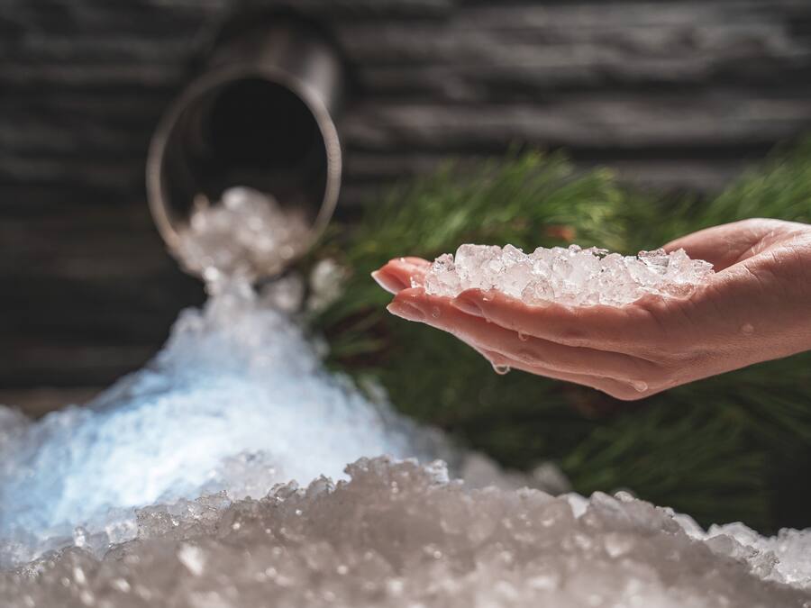 A hand holding salt crystals with a salt shaker in the background.
