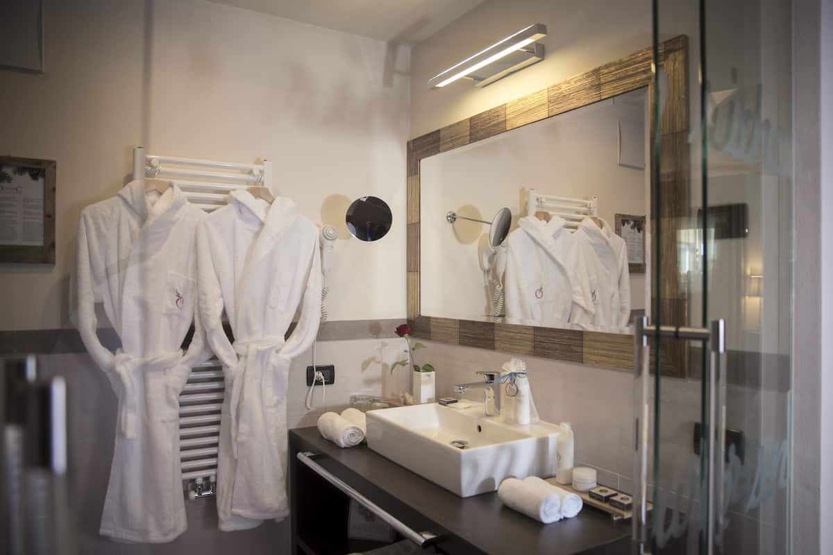 Un baño moderno con un espejo grande, un lavabo y dos albornoces blancos colgados en un perchero.