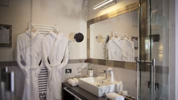 A modern bathroom with a large mirror, a sink, and two white robes hanging on a rack.