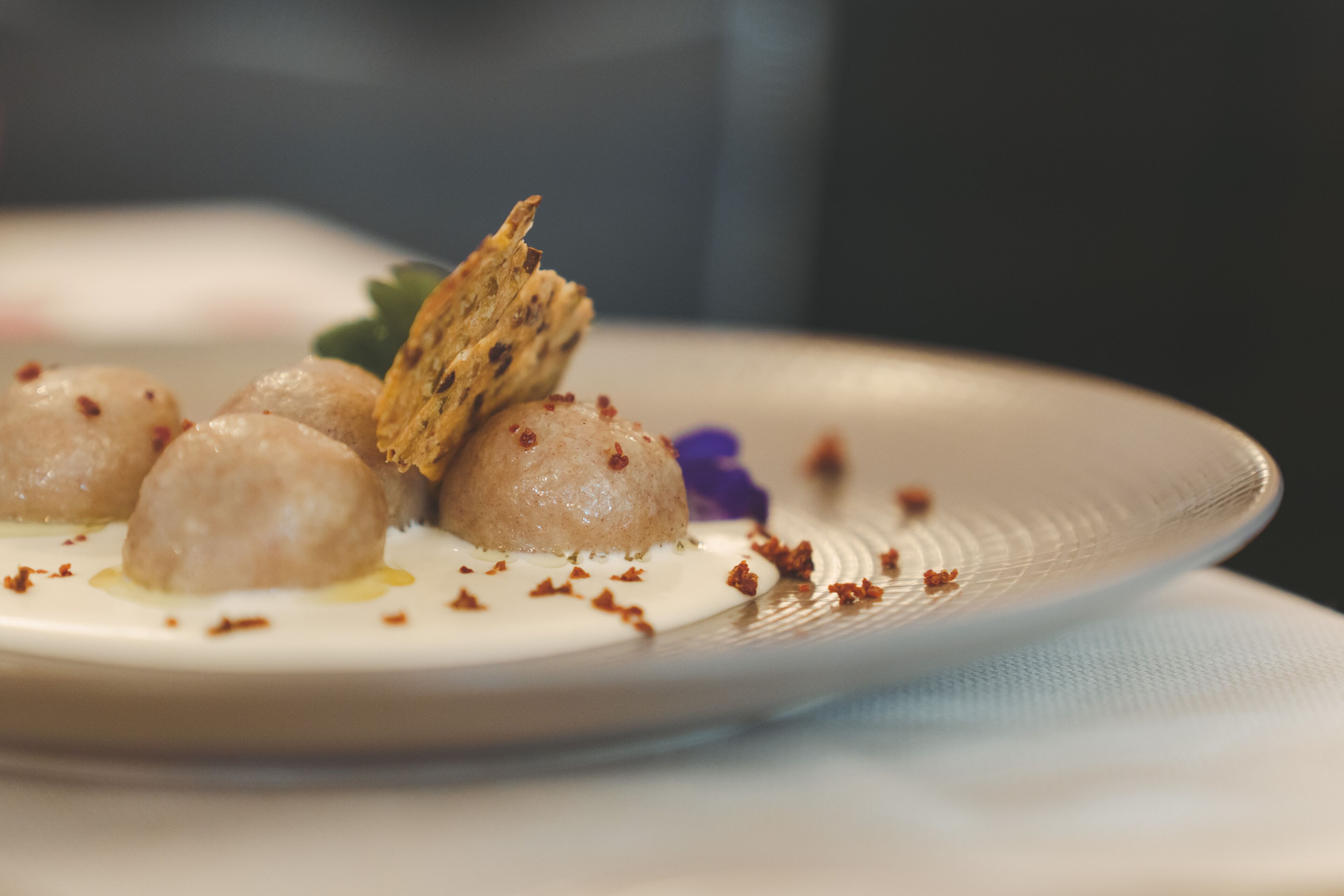 A plate of food with a creamy sauce, garnished with a purple flower and crispy elements.