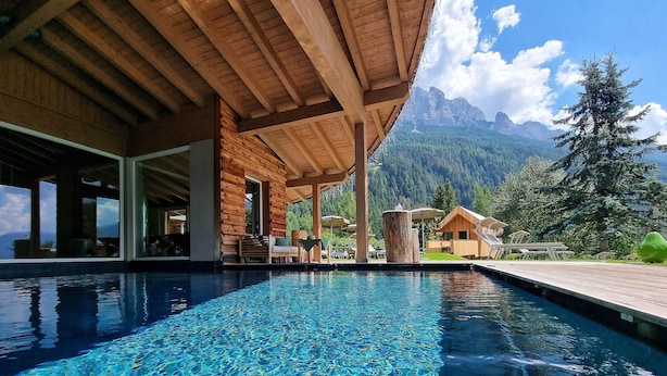 Une piscine à l’eau claire, une terrasse en bois et une vue sur la montagne.