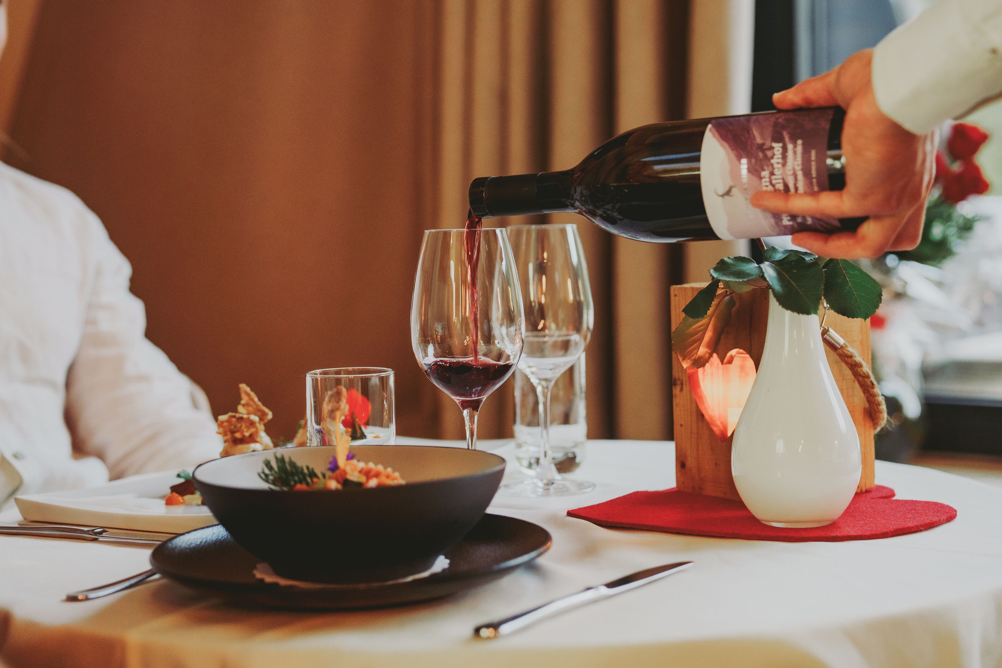A dining table with a bowl of food, wine glasses, and a bottle being poured into one of the glasses.