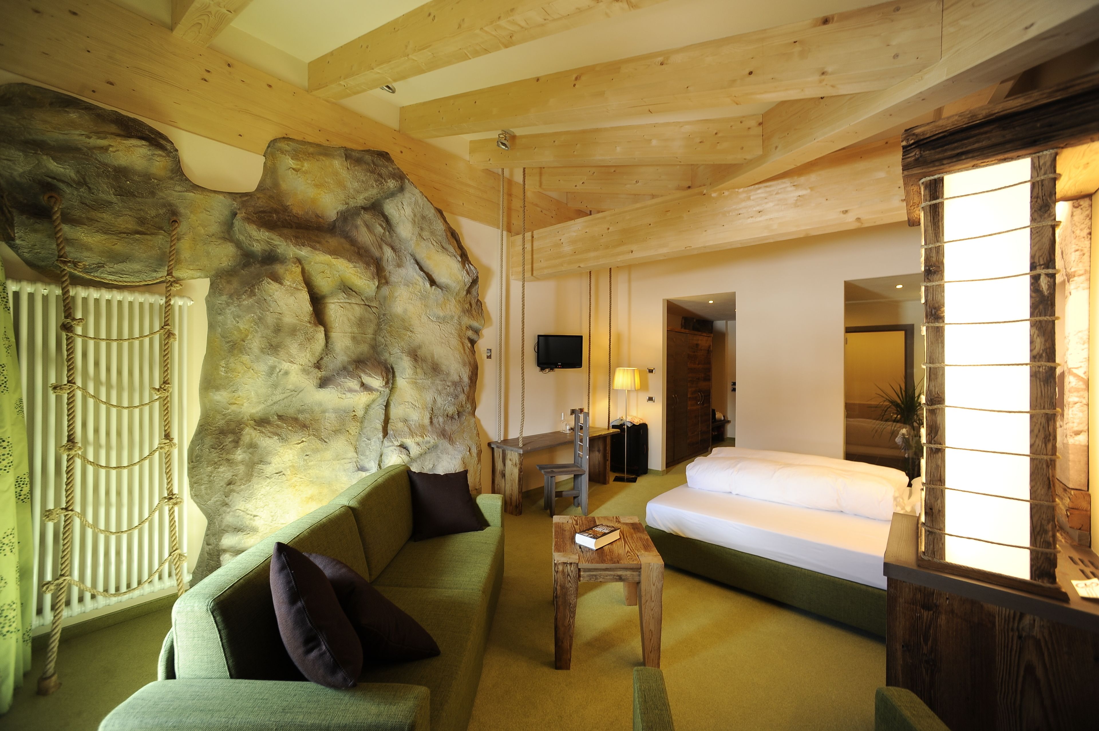 A room with a large rock feature, a bed, a sofa, a small table, and a wooden ceiling.