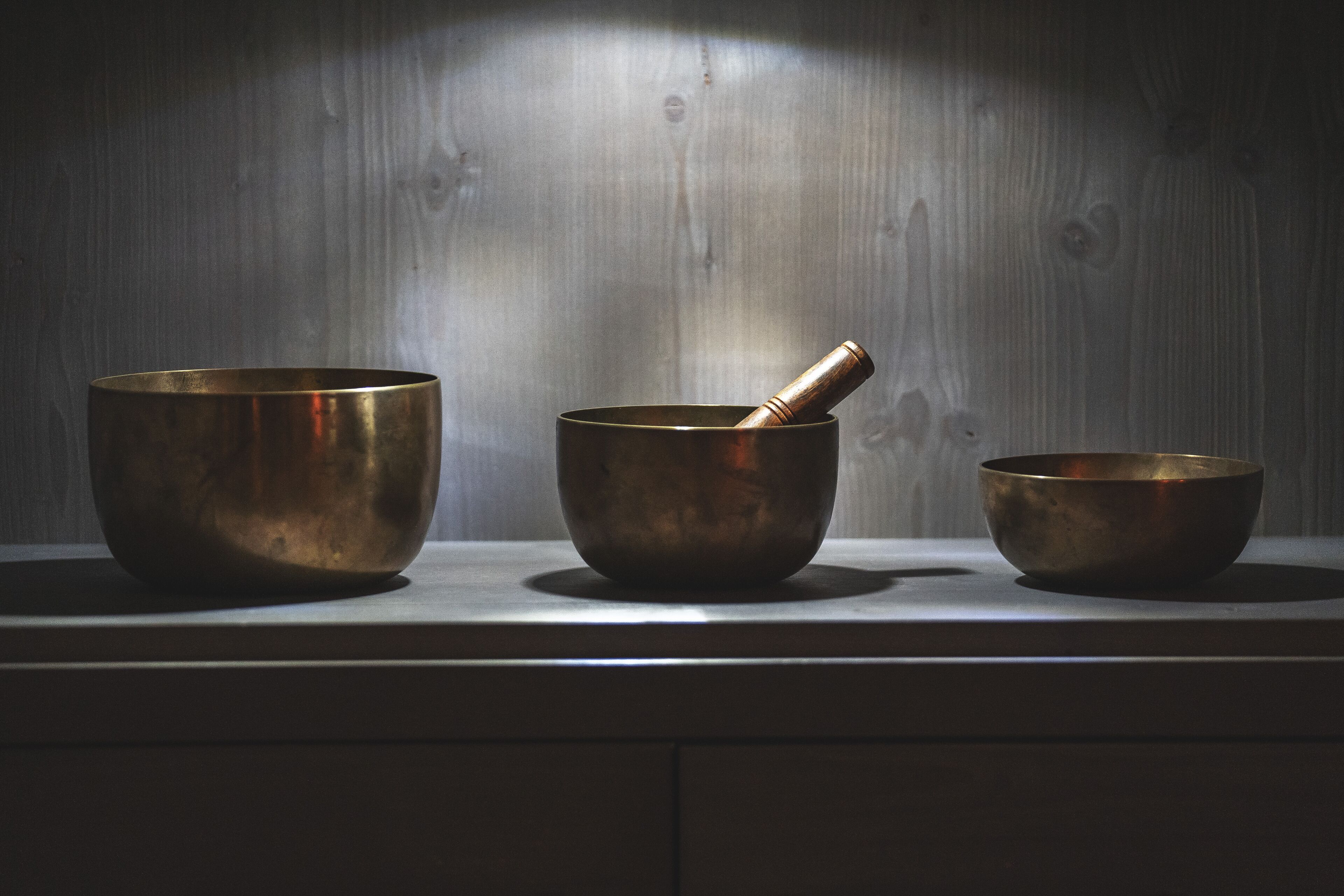 Three brass bowls on a wooden shelf against a wooden wall.